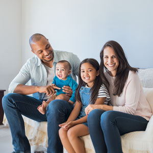 A family of four sits together on a couch, enjoying quality time with their young child - Gomez Law PLLC.