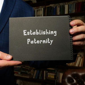 Businessman holding notebook with "establishing paternity" written on it. - Gomez Law PLLC.