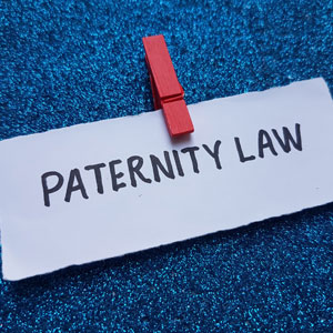 Paper with 'Paternity Law' clipped by a red peg on a blue glitter background - Gomez Law PLLC